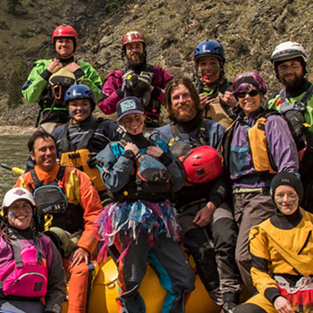 Group photo of rafters in gear standing beside a river.