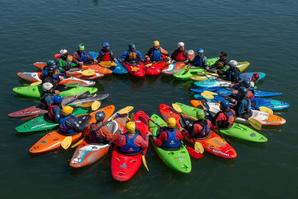 rainbow array of whitewater kayakers in a circle