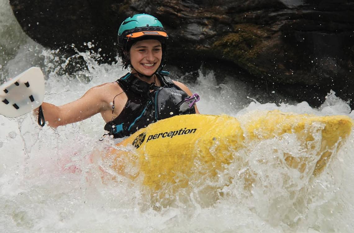 Action shot of Chloe Sligh whitewater kayaking with hand paddles.