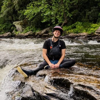 Profile photo of Danielle Sartori sitting in whitewater kayaking gear by the Chattooga River.