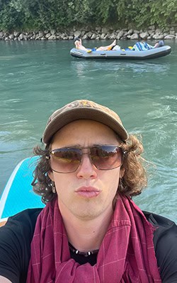 Selfie of Dylan on a stand up paddle board floating in blue water.