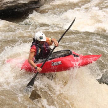 Madeline Bond whitewater kayaking in a red Dagger Kayak.