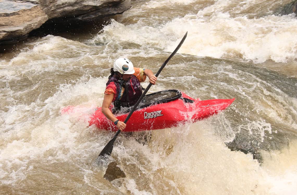 Madeline Bond whitewater kayaking in a red Dagger Kayak.