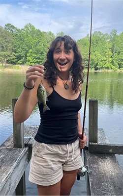Madeline Bond holding a fish by the lake.
