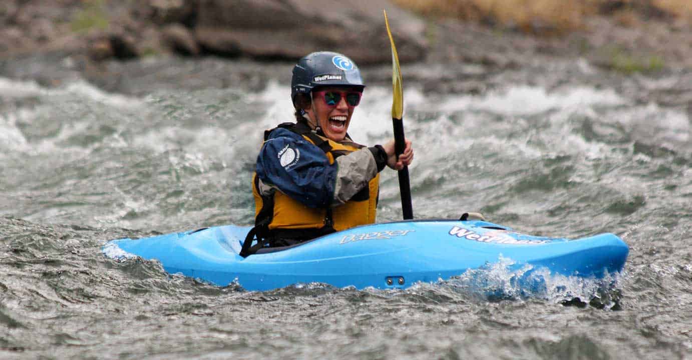A woman smiles while kayaking on a beginner river kayaking course. Wet Planet Whitewater in Washington Oregon Idaho