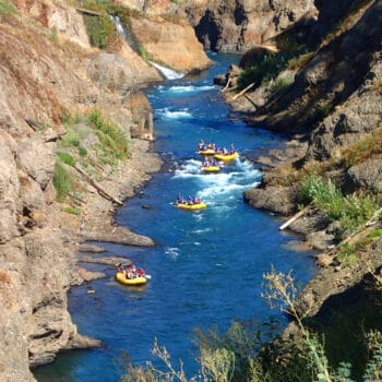 A view from above of rafts floating past a waterfall in a canyon on the White Salmon River