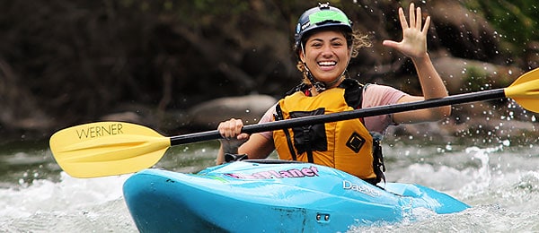 An image of a female kayaker smiling and waving at the camera.