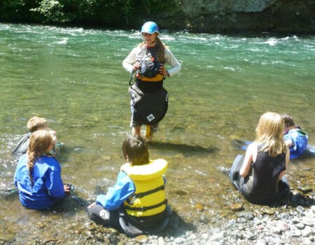 Person standing in a river talking to five kids