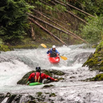 A kayak instructor watches a student run a rapid during a private kayak lesson