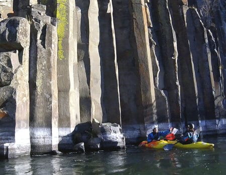 Two kayakers on the river in front of columnar basalt