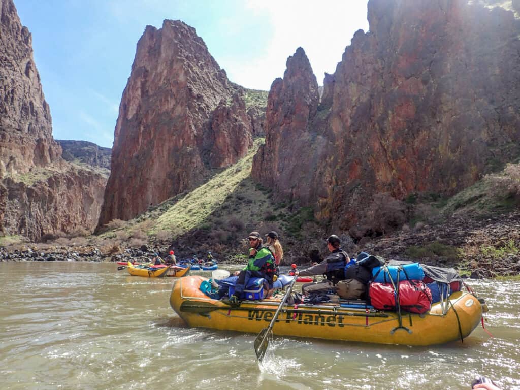 One rower and two passengers float in a gear raft with beautiful Owyhee River canyon scenery in the background.