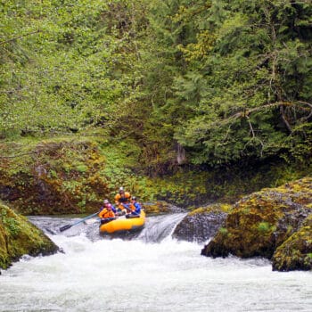 A loan raft on a Hood River rafting trip runs a rapid with beautiful scenery in the background.