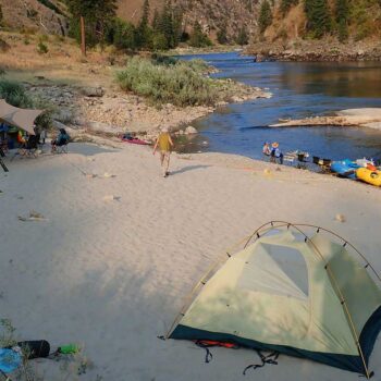 A tent is set up on the beach with rafts floating in the Main Salmon River in Idaho.