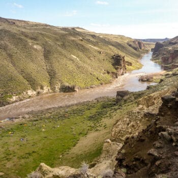 A scenic view taken from up high shows an impressive view of the Owyhee River canyon in Oregon and a a group of tents at camp along the river bank.