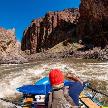 Seen from the back of the raft, a rafter rows a raft through a rapid in one of the canyons on the Owyhee River rafting trip.