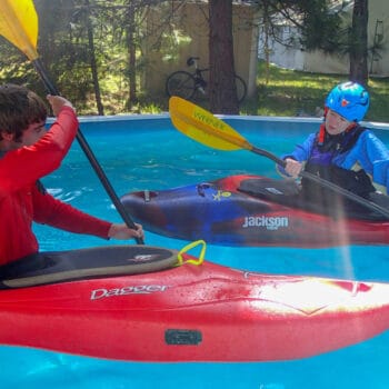 During a kayak pool session course, an instructor demonstrates stroke techniques to a student.