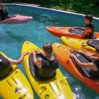 Students in kayaks listen to their instructor explain technique while floating in the pool during a kayak instruction course.