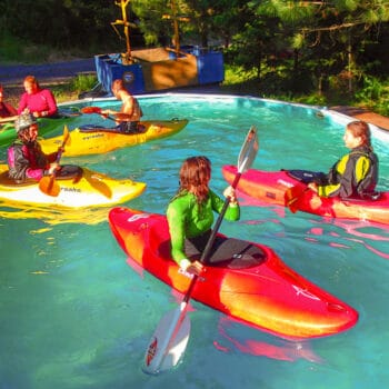 Four kayakers paddle in the pool on a Wet Planet kayak instruction course.