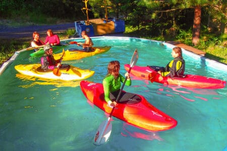 Four kayakers paddle in the pool on a Wet Planet kayak instruction course.