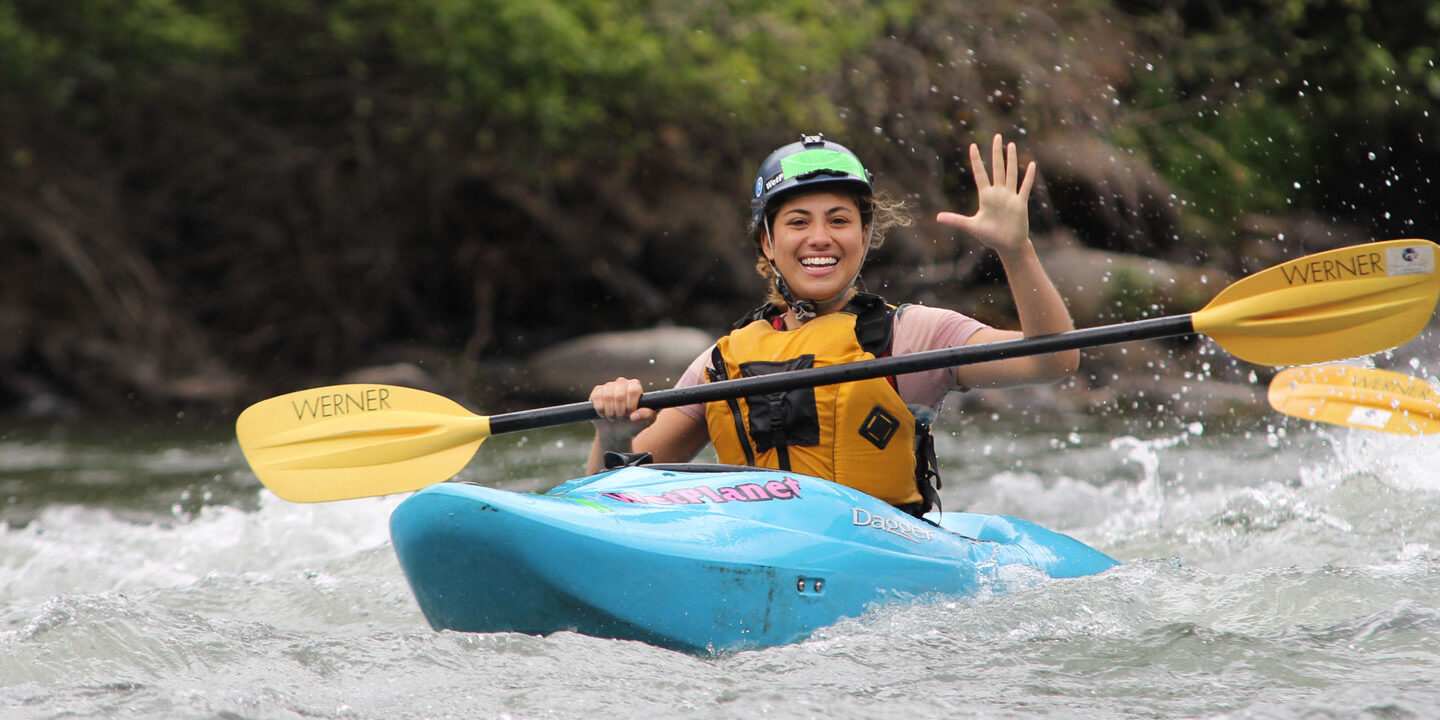 Kayak student smiling and waving on the river