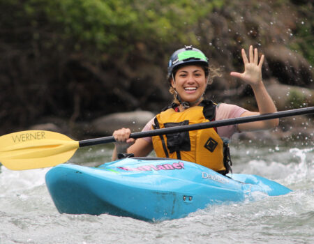 Kayak student smiling and waving on the river