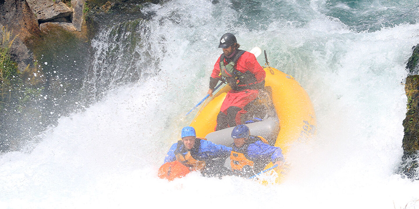 Three people in a raft going down a waterfall
