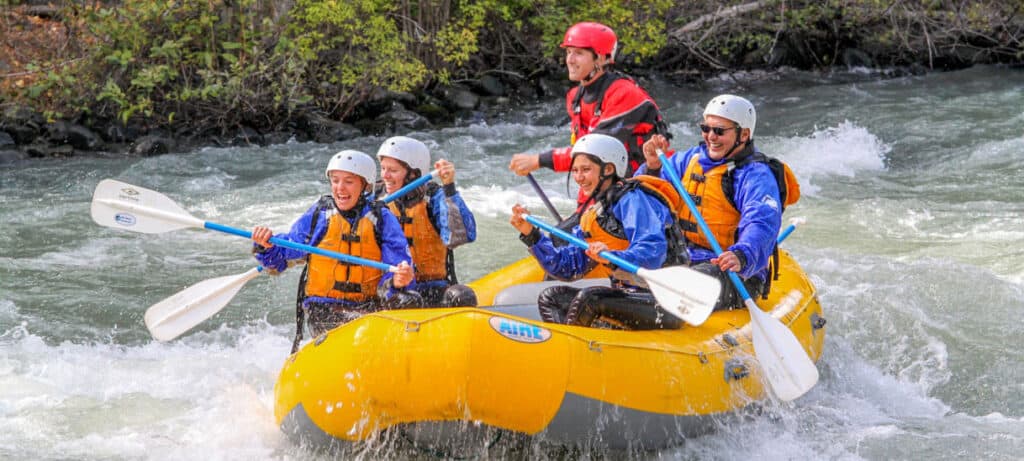 a group of rafters with their paddles up as they go over rapids on the tieton river
