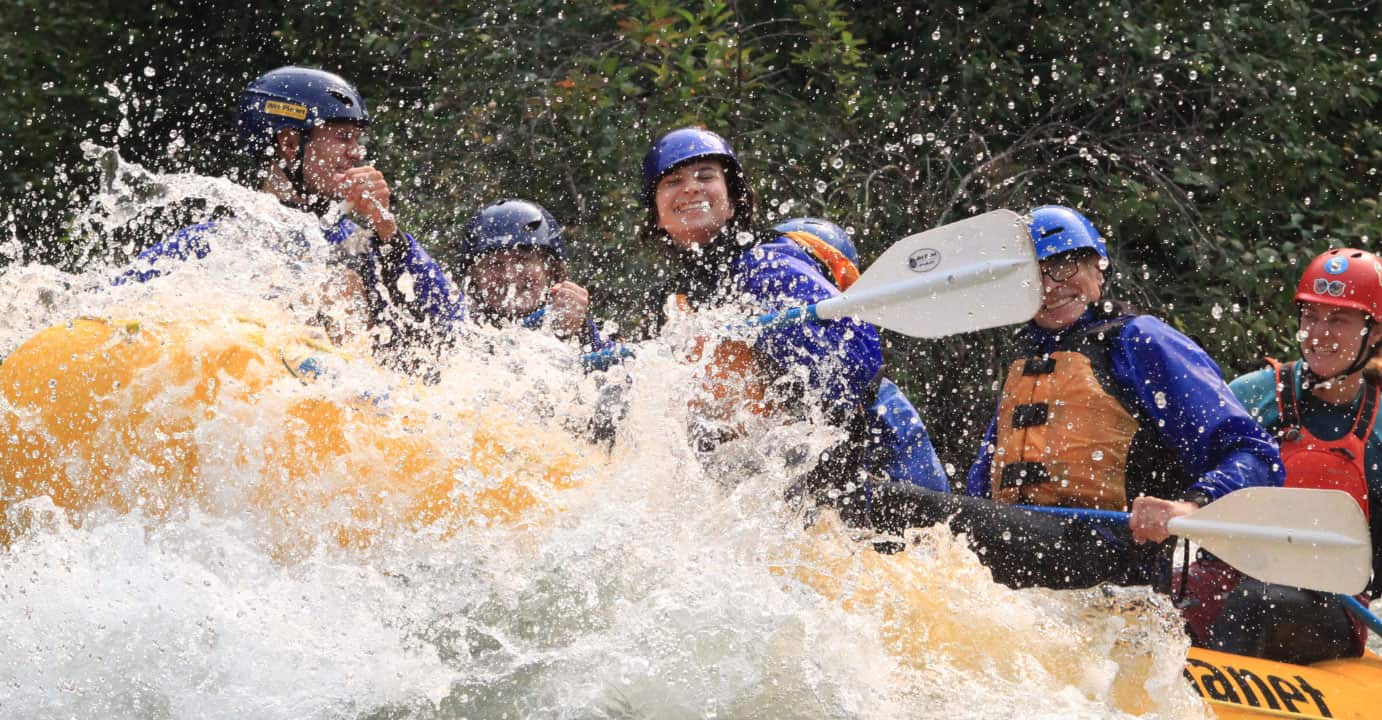 a group of rafters covered by a big water splash over their boat. Wet Planet Whitewater