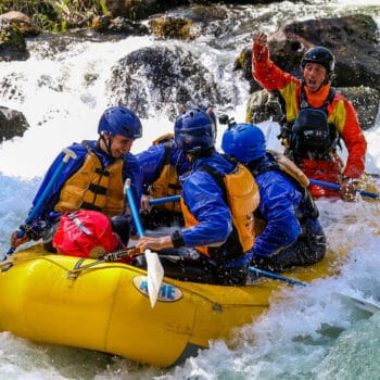 A raft guide holds his arm in the air in celebration while running a rapid on a white salmon river rafting trip.