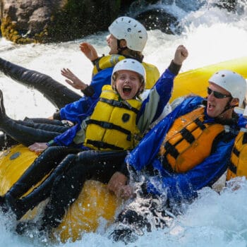 A young boy on a rafting trip holds his arm in the air in celebration while his family holds onto the front of the raft in the middle of a rapid on the White salmon river.