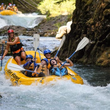 A group of rafters on a White Salmon river rafting trip celebrate with paddle high-fives while running a rapid.