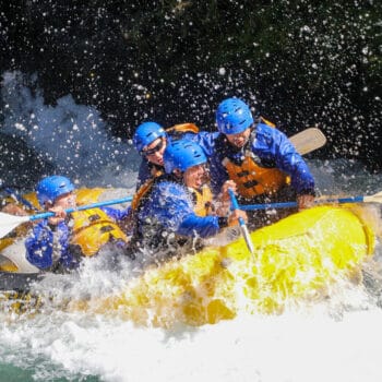 A group of rafters on a river rafting trip is splashed with waves while paddling through Top Drop rapid on The White Salmon River in Washington.