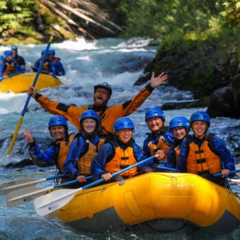 A raft guide celebrates iand the paddlers wave to the camera on a White Salmon river rafting tip in Oregon and Washington.