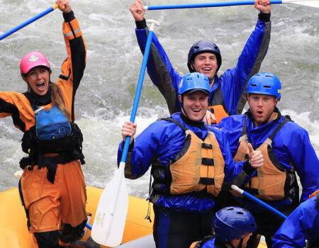 People holding up their paddles and smiling on a raft going down a river