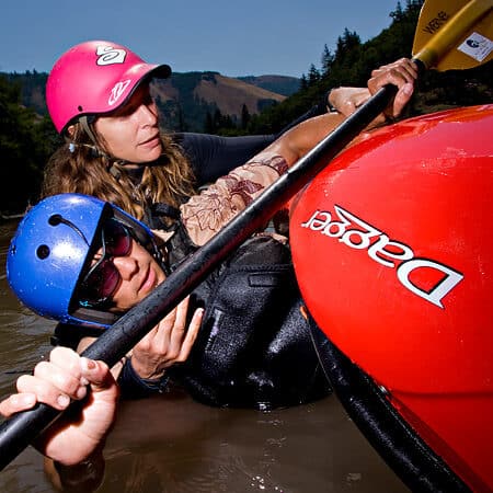 A kayak instructor on an ACA instructor course holds a student's head while teaching him to roll a kayak.
