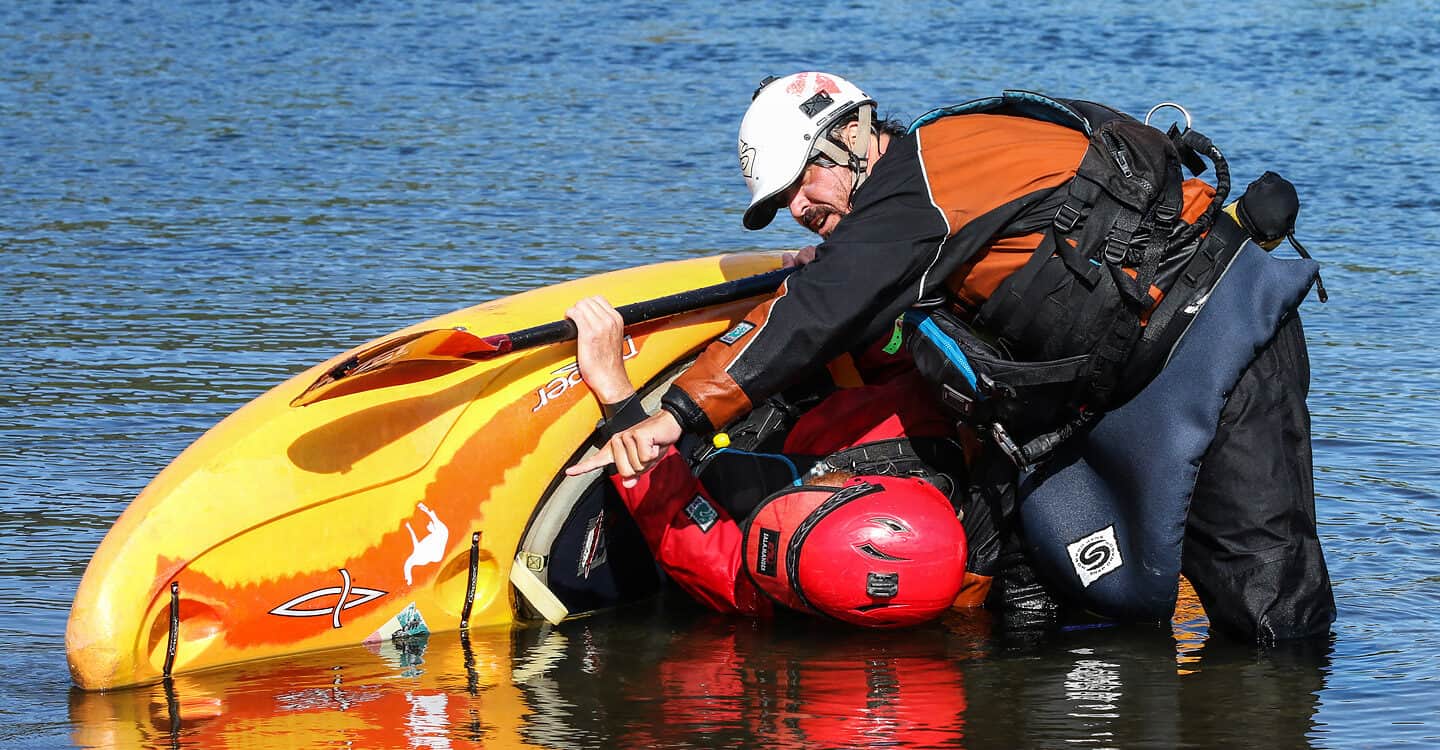 An instructor stands in the water and holds a student practicing a kayak roll during an ACA kayak instructor course.