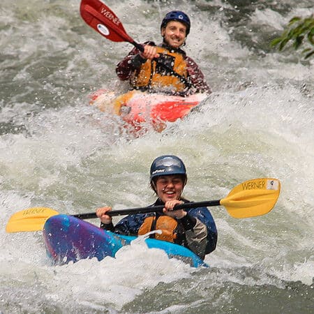 Two kayakers paddle through a rapid on a beginning river kayaking course.