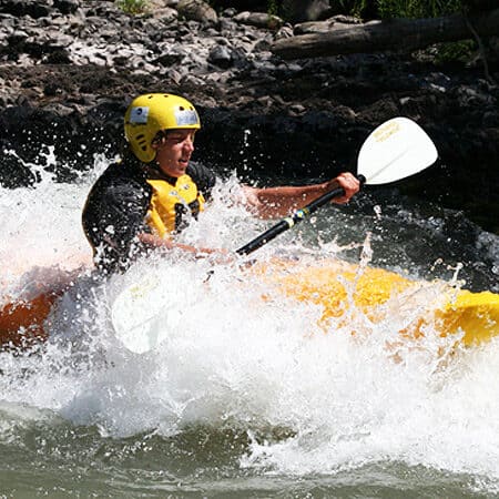 A kayaker splashes through a wave on a beginner river kayaking lesson.
