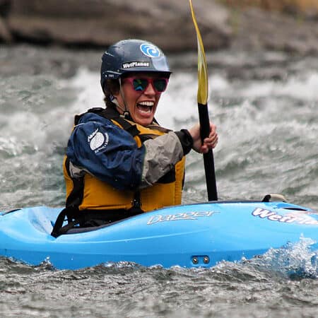 A woman smiles while kayaking on a beginner river kayaking course.
