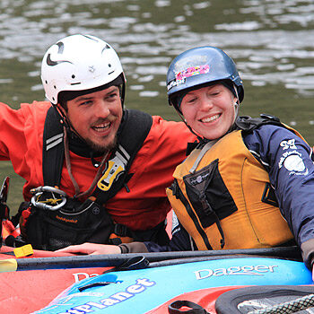 An instructor and a student sit in their kayaks and smile at the camera on a Washington and Oregon beginner kayak instruction course.