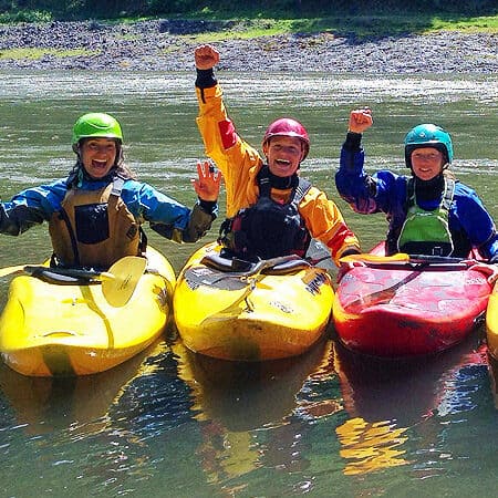 Three female kayakers post together and celebrate in their kayaks.