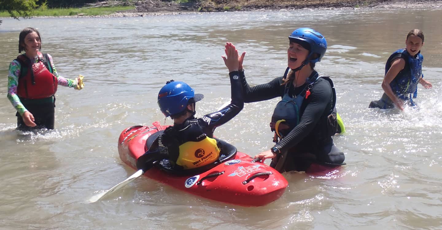 Female kayak instructor gives high five to child during the kids kayak course. Wet Planet Whitewater in Washington, Idaho, Oregon