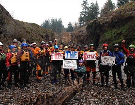 Group of people holding "Free the Rivers" signs in front of a dam removal site