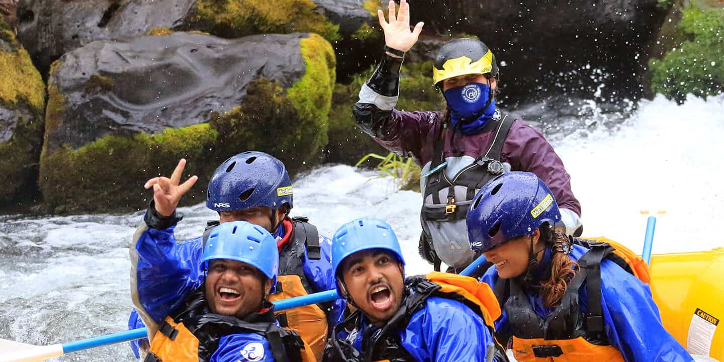 A raft guide waves to the camera while wearing a facemask.