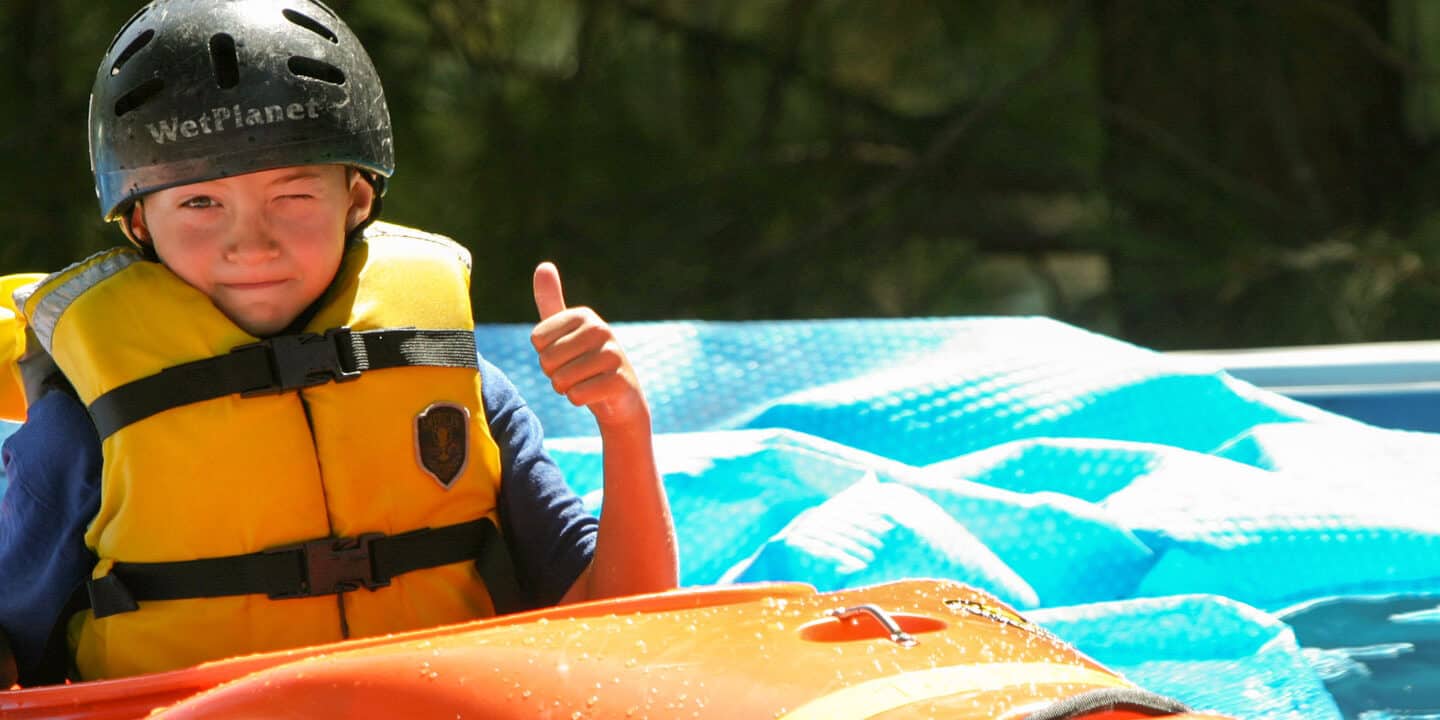 Young boy gives a thumbs up during his kayak trip on the river. Wet Planet Whitewater in Washington, Idaho, Oregon