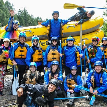 A group of rafters wearing silly outfits poses for the camera in front of a stack of rafts - Oregon and Washington river rafting with Wet Planet Whitewater.