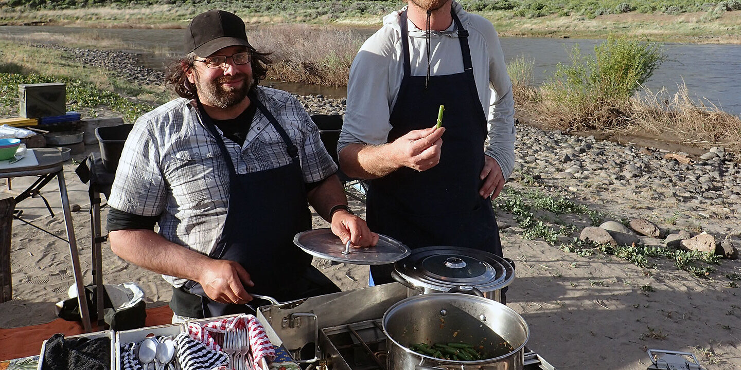 Two people cooking a group meal on a multi-day river trip