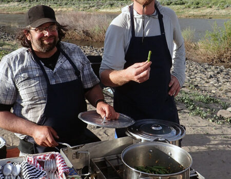 Two people cooking a group meal on a multi-day river trip