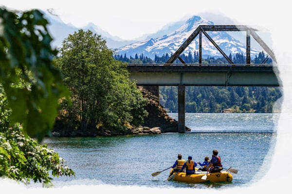 Rafters enjoy the view of a bridge and snow capped mountain during their float. Wet Planet Whitewater in Washington Oregon Idaho