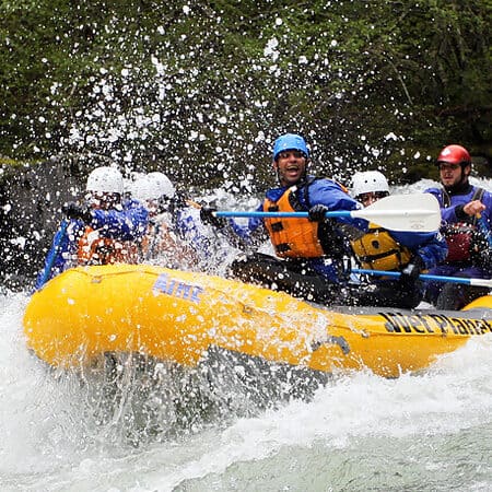 A rafting guest on a class V Hood River rafter trip smiles and celebrates while paddling through a large wave.